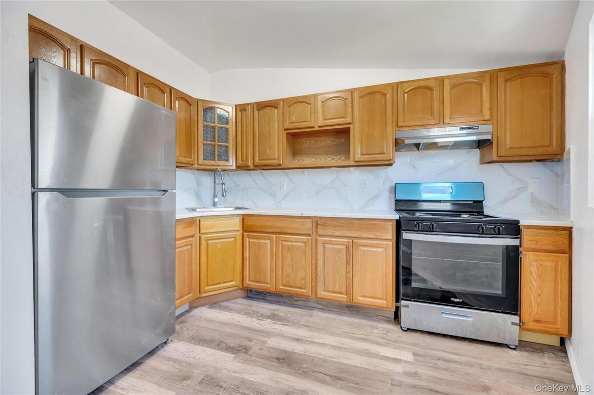 Kitchen featuring wood-finish cabinetry, stainless steel appliances, white countertops, and a full tile backsplash
