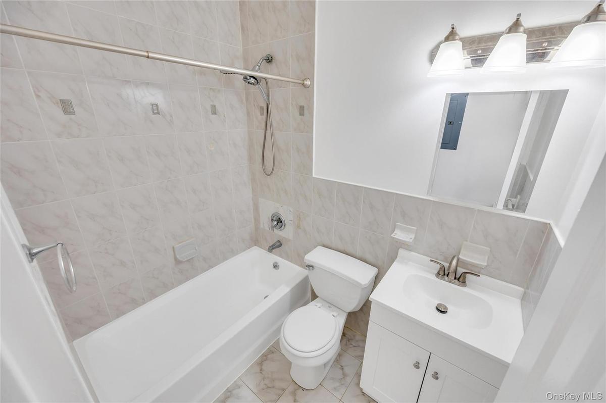Bathroom featuring a combination shower and tub with ceramic tile surround, a single vanity with storage, a wall-mounted mirror, and overhead vanity l