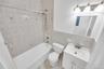 Bathroom featuring a combination shower and tub with ceramic tile surround, a single vanity with storage, a wall-mounted mirror, and overhead vanity l