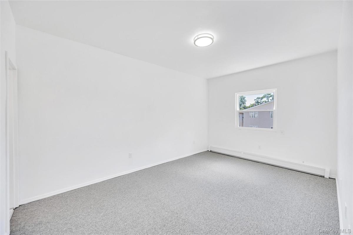 Bright room featuring a single window, white walls, gray carpet, a flush-mount ceiling light, and baseboard heating