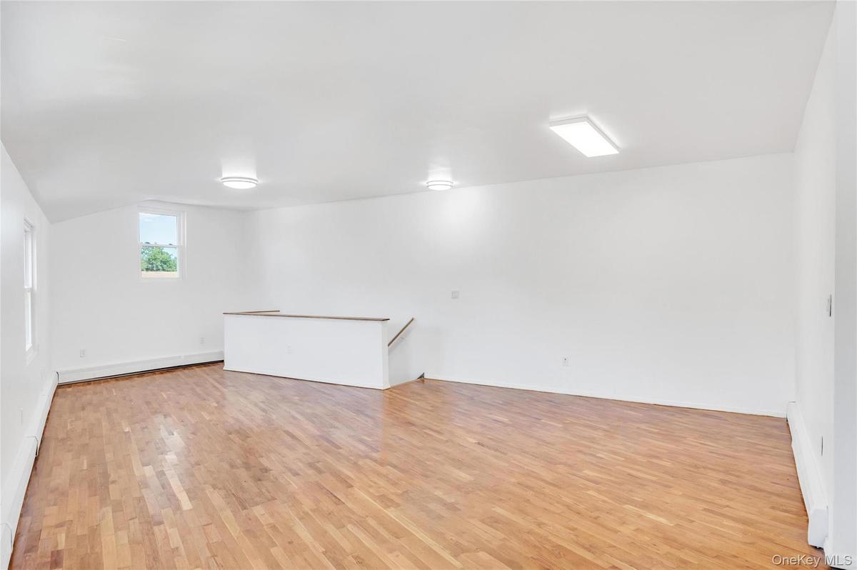 Spacious room featuring wood-finish flooring, white walls, and multiple windows