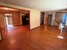 Expansive main living area featuring wood-finish flooring, a staircase with metal railings, and a doorway leading to a kitchen with dark cabinetry and
