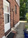 Brick exterior featuring a white storm door, decorative wrought iron handrail, and an exterior wall lantern