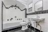 Bathroom with full bathtub, wall-mounted sink, and a black and white tile design