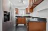 Stainless steel refrigerator with a dispenser, black tile flooring, wood-finish cabinetry, dark speckled countertops, and a stainless steel sink with 