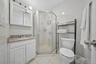 White tiled bathroom featuring a corner shower, white vanity with a light-toned countertop, and a mirrored medicine cabinet