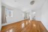 Bright and spacious room featuring gleaming wood-finish flooring throughout, abundant natural light from multiple windows with soft drapery, crisp whi