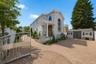 French Colonial residence showcasing a brick paver driveway and circular turret with arched windows