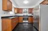 Kitchen featuring wood cabinetry, dark countertops, a stainless steel refrigerator, a range, and a stainless steel range hood