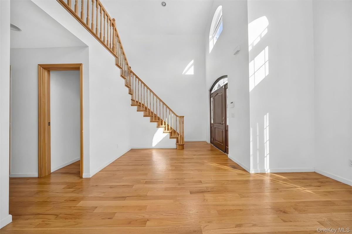 Two-story entryway featuring a wood-finish staircase with balusters, a dark wood-finish arched front door, and multiple high-set windows