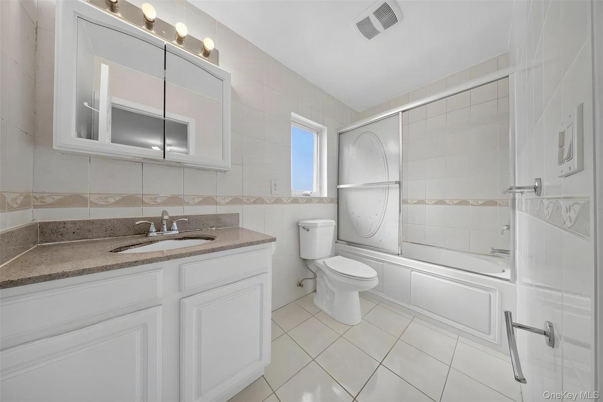 Spa-inspired primary bathroom featuring a white vanity with granite countertop, medicine cabinet with mirrored glass doors, ceramic tile flooring, and