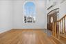 Bright, light-filled foyer showcasing warm wood-finish flooring, an arched transom window with natural light, and an elegant wooden staircase with dec