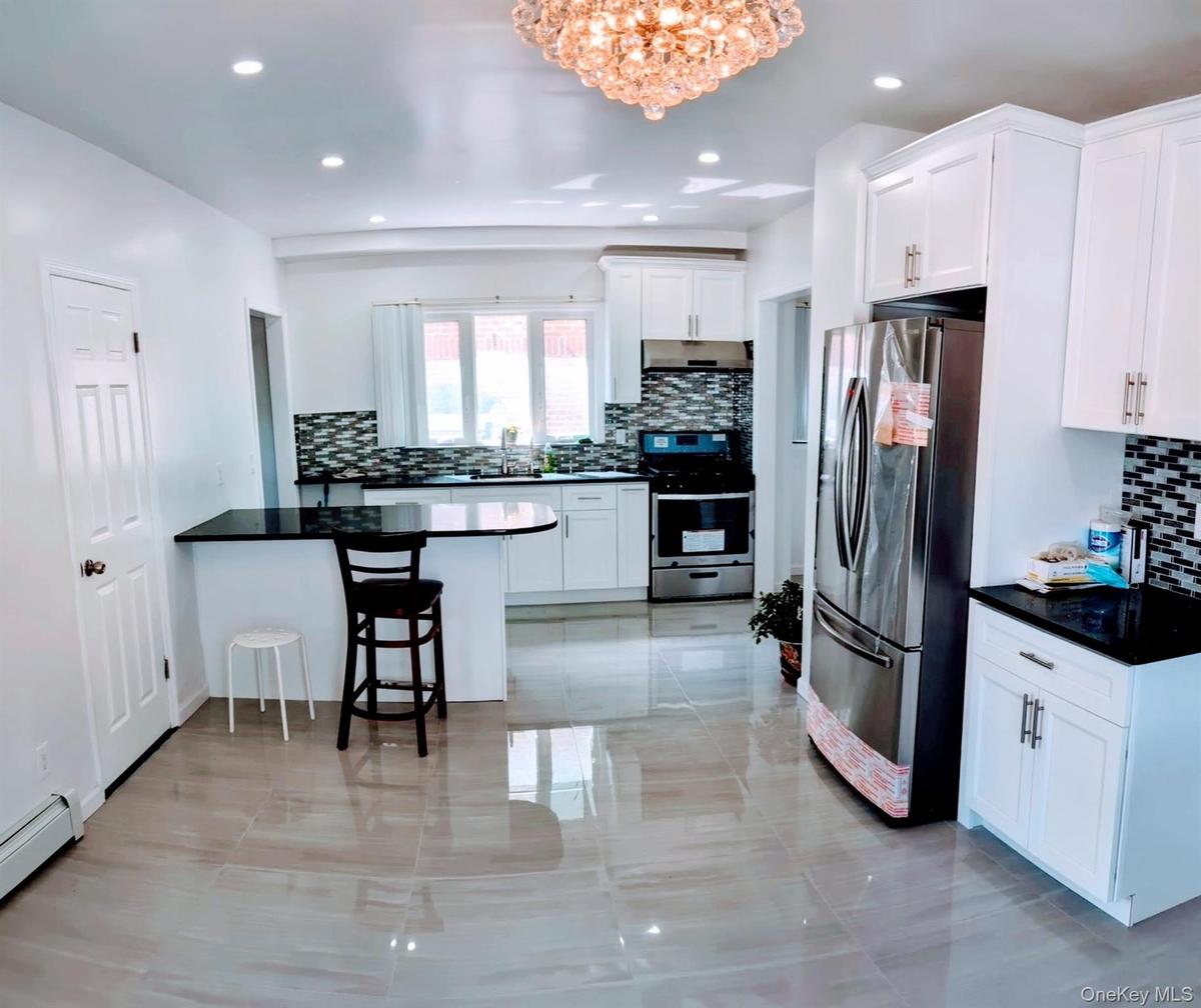 Kitchen with a peninsula, a chandelier, stainless steel appliances, a baseboard radiator, and decorative backsplash