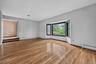 An expansive, formal step-down living room with soaring high ceilings, freshly polished solid hardwood floors, and a large architectural bow window le