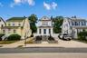 White clapboard exterior with an arched dormer, raised stone planter beds, and a concrete driveway