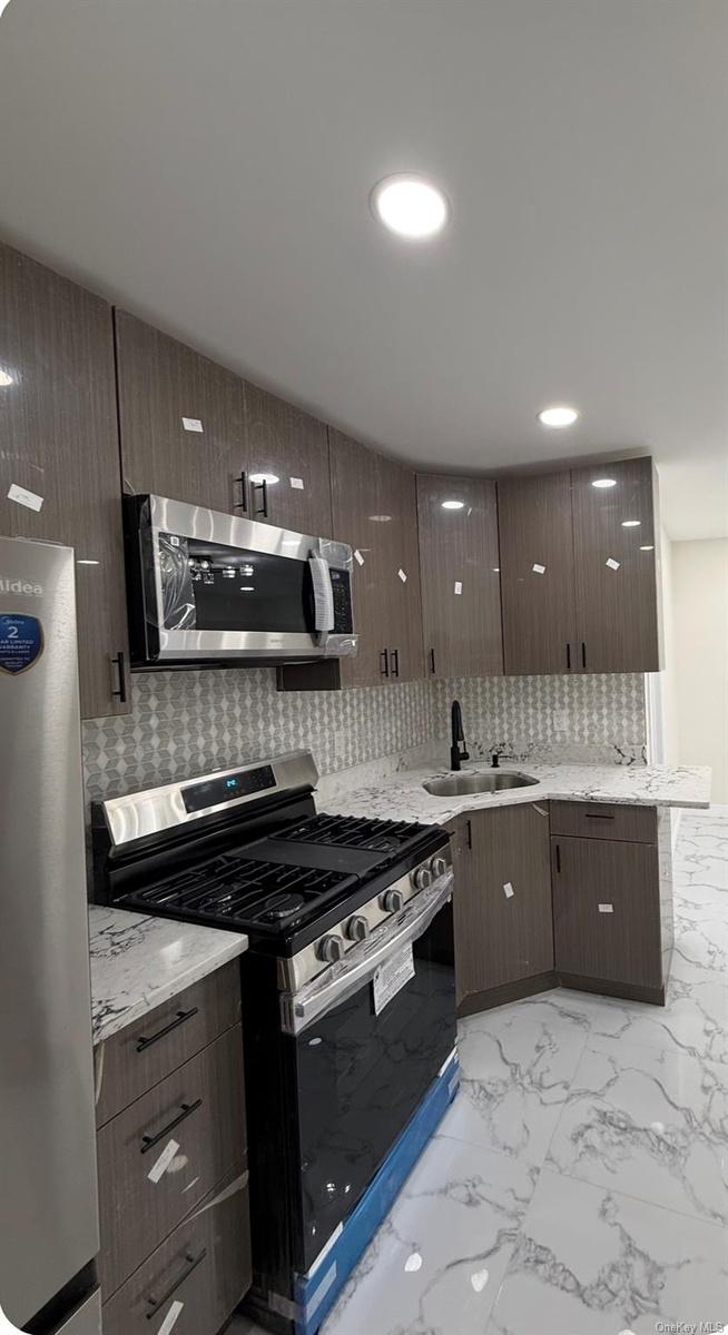 Kitchen featuring wood-finish cabinetry, stainless steel appliances, patterned tile backsplash, and light-toned countertops