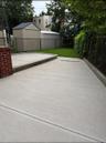 Expansive concrete patio with integrated drainage, brick pillar, and separate lawn area