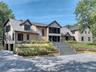 Shingle-style exterior with black trim windows, multi-level tiered landscaping, broad front steps, and a gravel driveway