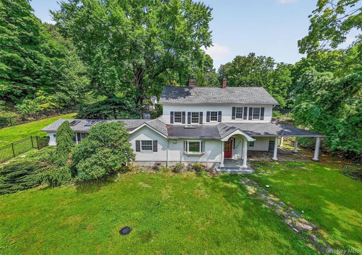Two-story residence featuring a covered front entry, an expansive side porch with columns, a stone pathway, and skylights on the single-story extensio