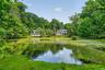 Expansive waterfront property with a white-sided two-story residence, surrounded by mature trees and lush green landscaping