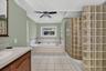 Recessed tub with tile surround, white tile flooring, ceiling fan, and curved glass block shower wall, Jetted Shower behind it.