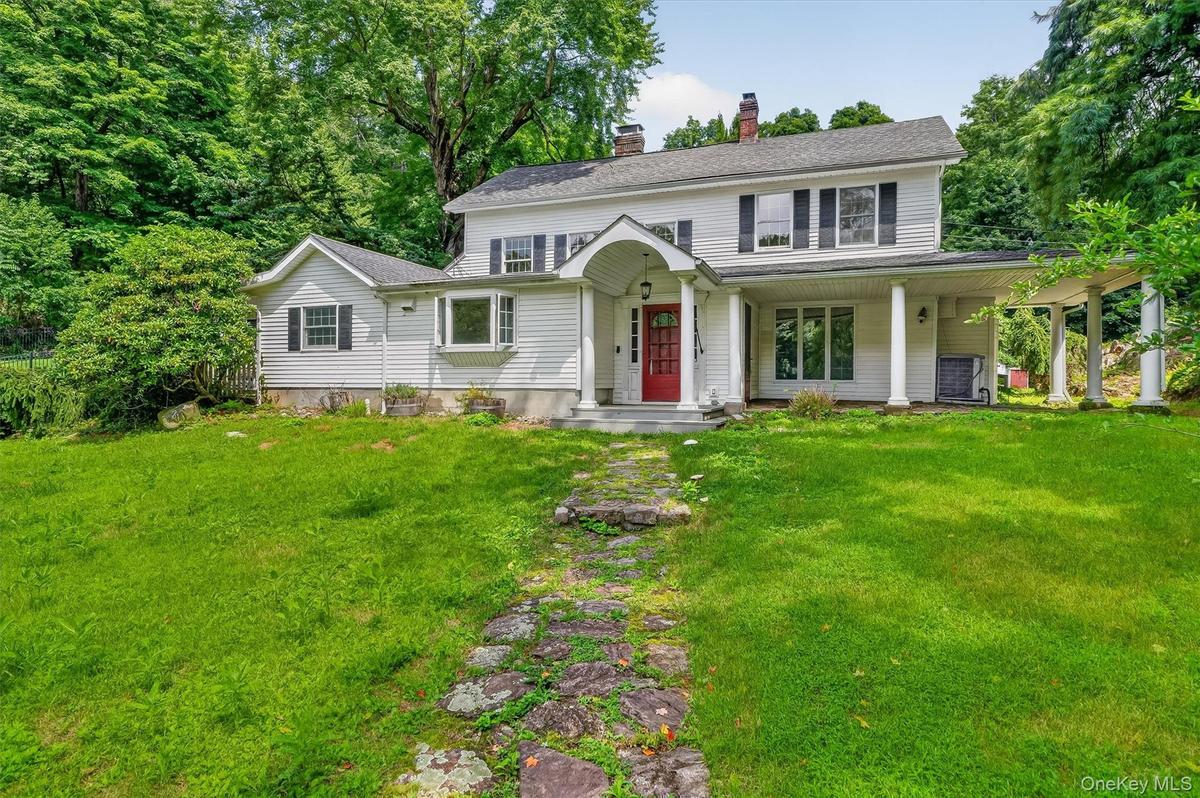 White siding exterior with a red entry door, covered front porch, columned side porch, and a bay window