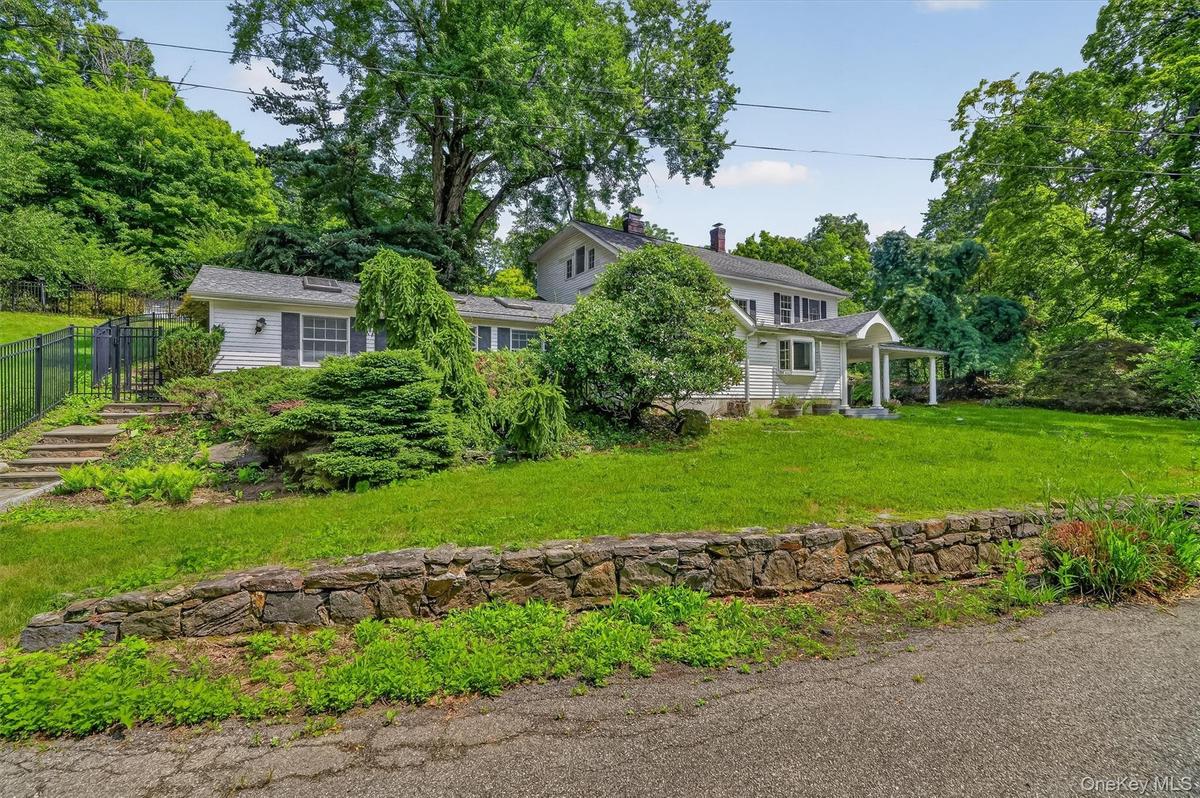 Expansive green lawn, mature trees, stone retaining wall, and a covered front porch with white columns