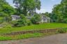 Expansive green lawn, mature trees, stone retaining wall, and a covered front porch with white columns