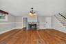 Hardwood flooring, stone fireplace, traditional chandelier, white staircase with dark wood treads, and white interior doors