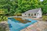 In-ground pool with protective cover, stone patio, and a cabana featuring a covered porch with white columns