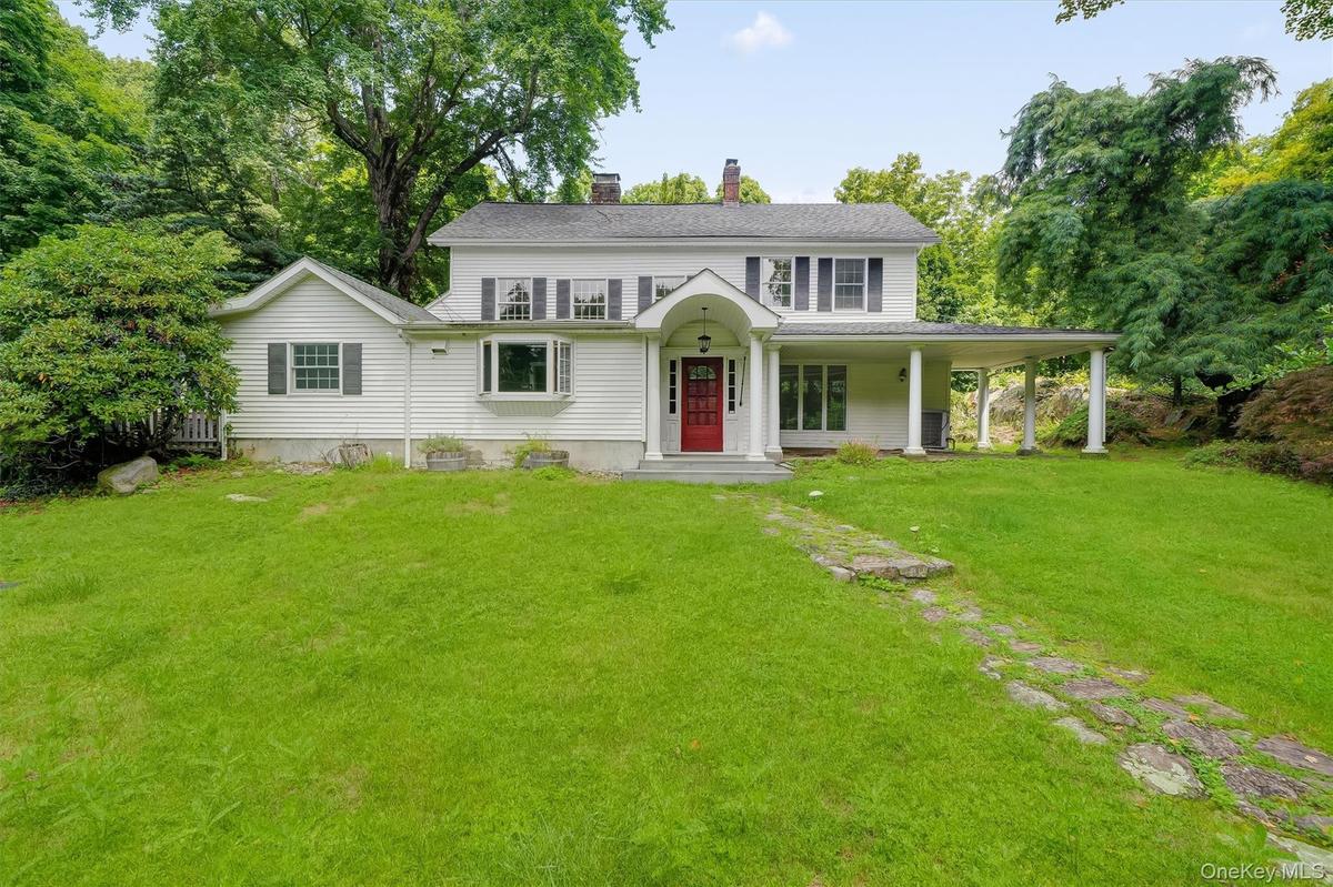 White siding exterior with a red entry door, covered front porch, bay window, and a stone pathway