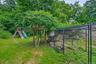 Lush backyard featuring a wooden playset with a slide, a gazebo structure with natural wood posts, and a fenced enclosure ( Chicken Coup)