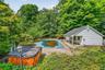 Outdoor swimming pool with surrounding stone patio, white siding pool house with covered porch, and wood-sided hot tub