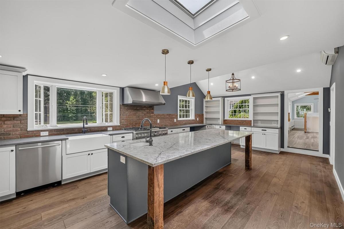 Kitchen featuring a center island with a stone countertop, wood-finish flooring, a farmhouse sink, chef grade stainless steel appliances, and a skylig