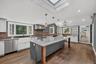 Kitchen featuring a center island with a stone countertop, wood-finish flooring, a farmhouse sink, chef grade stainless steel appliances, and a skylig