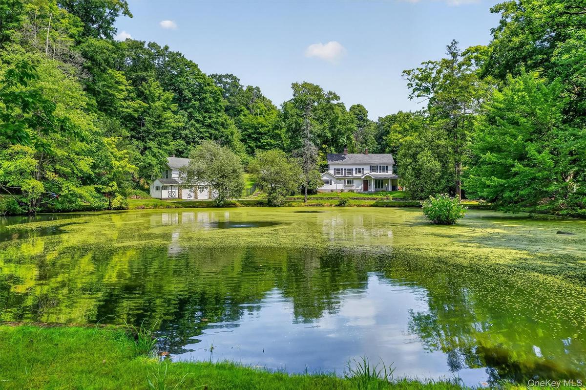 Private property featuring a traditional-style home with a columned porch, surrounded by mature trees and lush landscaping and your own pond.