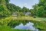 Private property featuring a traditional-style home with a columned porch, surrounded by mature trees and lush landscaping and your own pond.