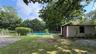 Fenced swimming pool, detached stucco structure, mature trees, green lawn, natural rock elements