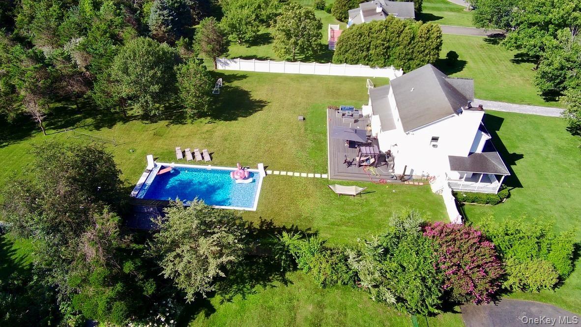 Expansive green lawn featuring an in-ground swimming pool, a large outdoor patio, mature trees, and a white picket fence.