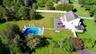 Expansive green lawn featuring an in-ground swimming pool, a large outdoor patio, mature trees, and a white picket fence.