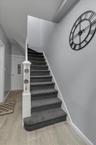 Elegant staircase featuring charcoal gray carpeted treads with white trim, ornamental newel post, and chrome handrail.