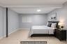 Spacious basement guest room featuring neutral gray walls, recessed ceiling lighting, and light wood-finish flooring.