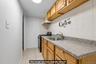 Galley kitchen featuring wood-finish cabinetry, speckled stone countertops, stainless steel sink with faucet, ceramic tile backsplash, and tile floori