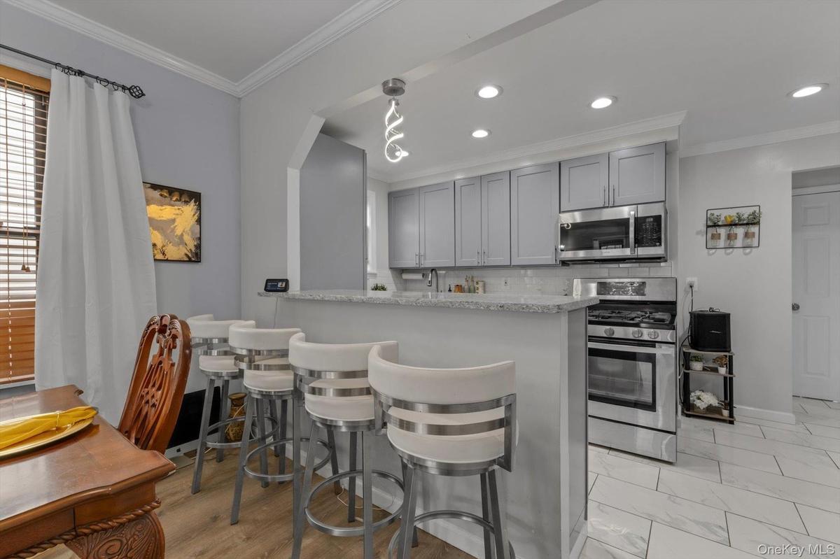 Kitchen featuring light gray cabinetry, stainless steel appliances, recessed lighting, and a breakfast bar.