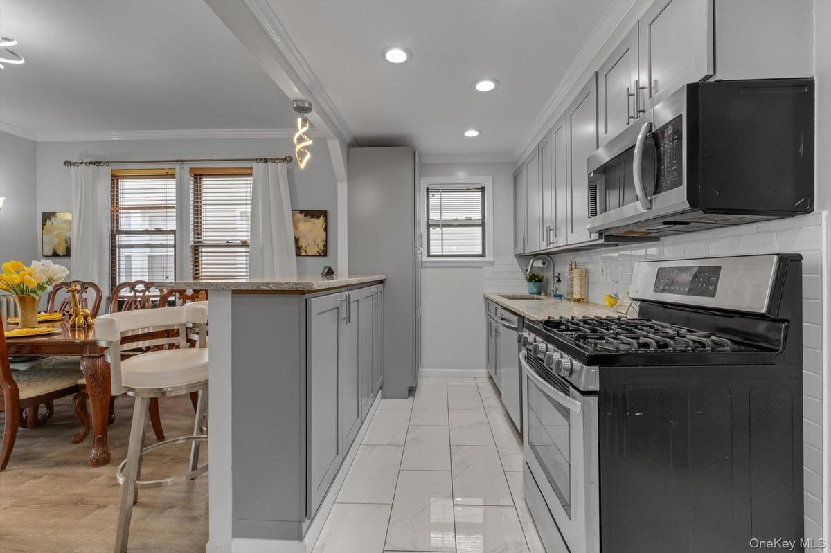 Galley kitchen featuring gray cabinetry, stainless steel gas range with overhead hood, tile flooring, recessed ceiling lighting, and a pass-through op