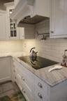 Kitchen featuring premium range hood, light stone counters, decorative backsplash, and white cabinets