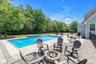 In-ground swimming pool with stone coping, paver patio, stone fire pit, and black fencing