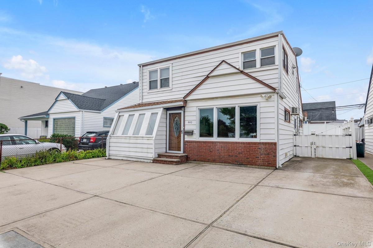 Two-story residence featuring white siding and a brick base, large driveway