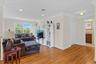 Bright, open living area showcasing hardwood flooring throughout, abundant natural light from large windows, white cabinetry with shelving and media s