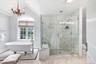 Clawfoot soaking tub, glass-enclosed shower with marble-look tile, arched window, chandelier, and a mosaic tile floor accent